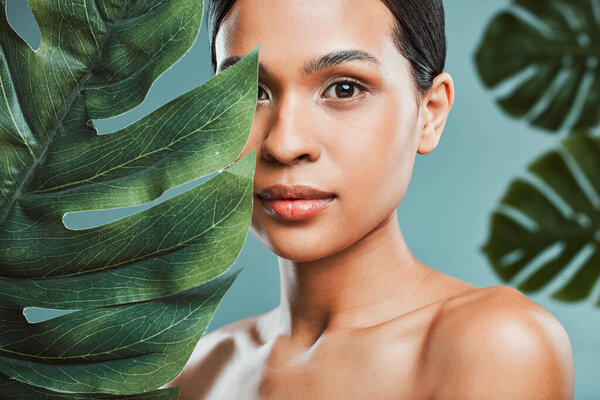 Studio portrait of an attractive young mixed race woman posing with a leaf against a green background. Latin female posing with a plant with her smooth soft skin.