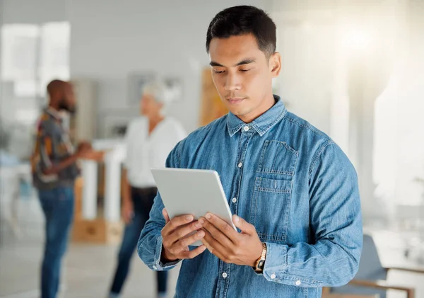 Serious asian businessman holding and using a digital tablet at work. Chinese male businessperson working on a digital tablet at work. Business professional using social media and browsing online.