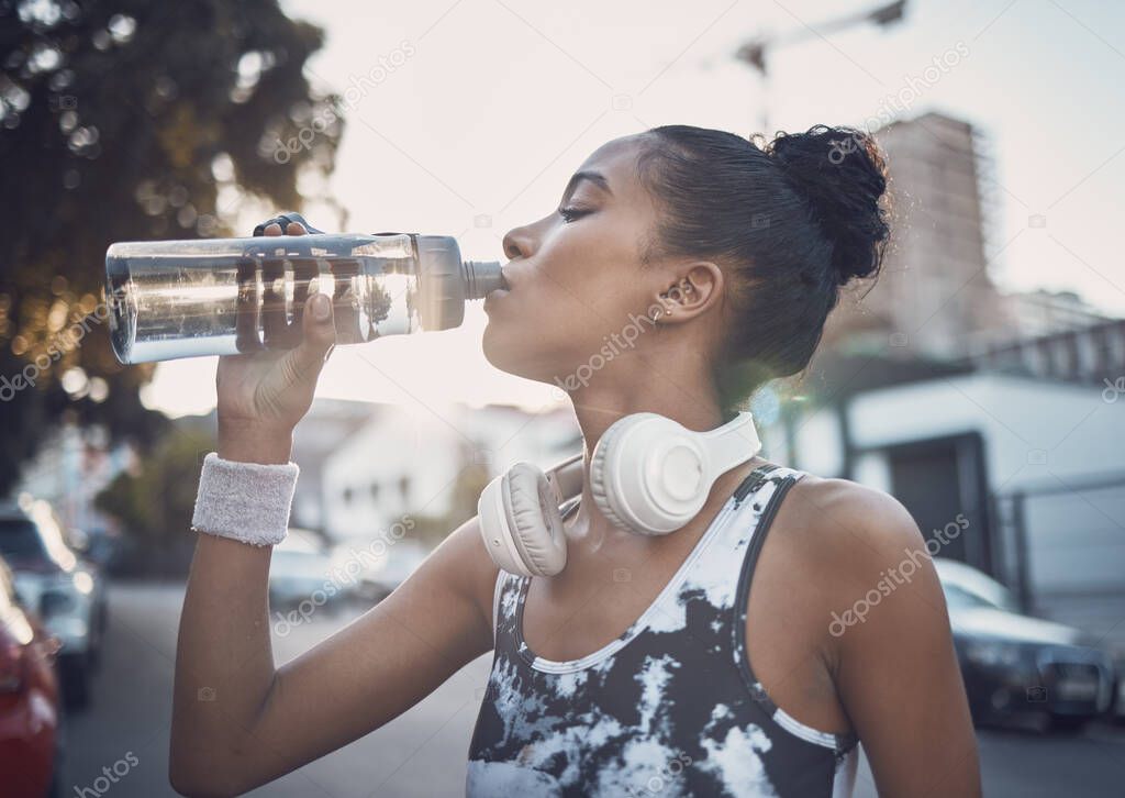 One fit young mixed race woman taking a rest break to drink water from a bottle while exercising outdoors. Female athlete quenching thirst and cooling down after running and training workout in the