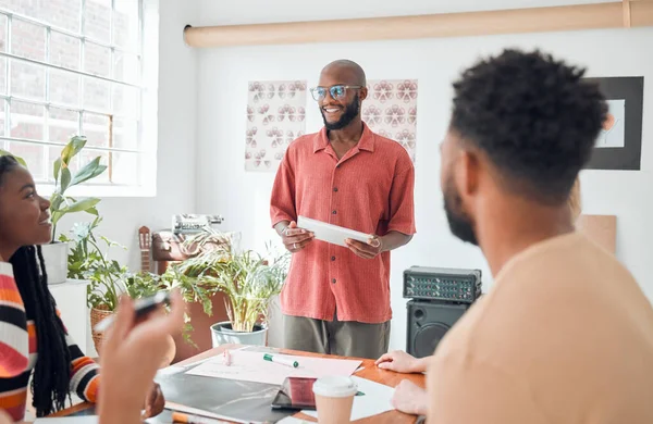 Group of diverse businesspeople having a meeting in a modern office at work. Young happy african american businessman wearing glasses doing a presentation of an idea using a digital tablet in a