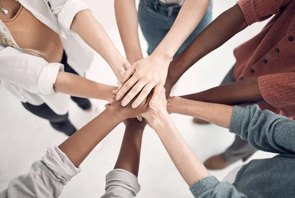 Group of diverse businesspeople piling their hands together in an office at work. Business professionals having fun standing with their hands stacked for support and unity from above.