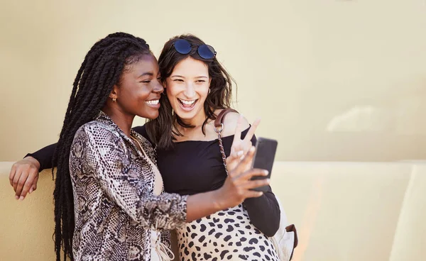 Best friends having fun and showing peace sign while taking selfie outdoors. Two multiethnic female friends spending time together in city and taking photos for social media on smartphone.