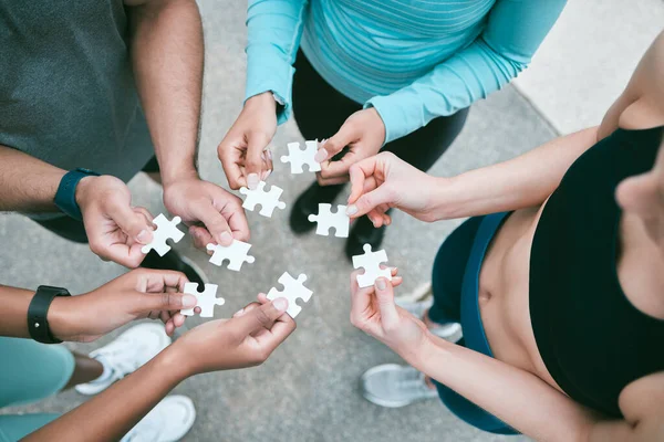 Closeup of diverse group of people from above assembling jigsaw puzzle pieces together. Hands of multiracial people working in synergy to problem solve. Using dedicated teamwork to support and help