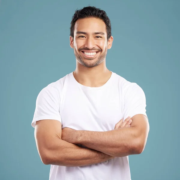 Handsome young mixed race man with his arms crossed while standing in studio isolated against a blue background. Happy hispanic male smiling while looking confident and powerful with his arms folded.