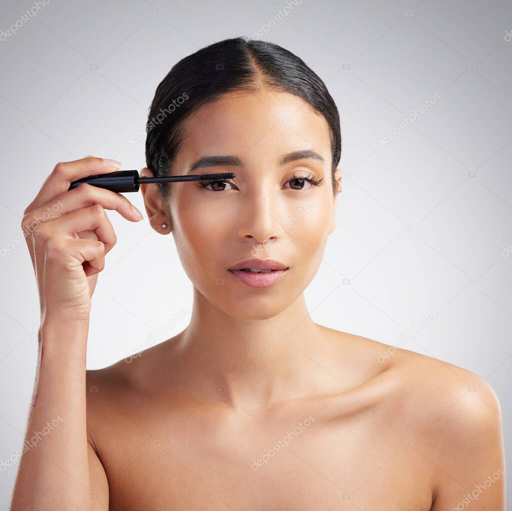 Studio portrait of a beautiful young mixed race woman with glowing skin posing against grey copyspace background. Hispanic woman with natural looking eyelash extensions applying mascara.