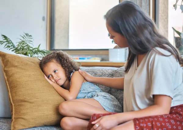 Sad depressed little girl lying on the couch and looking away while worried mother psychologist tries to talk to her. Loving caring mother trying to communicate with upset daughter. Young hispanic