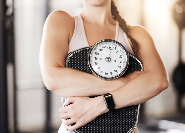 Closeup of one unknown caucasian athlete holding weight scale after workout in gym. Strong, fit, active woman maintaining diet during training and exercise in health and sport club. Healthy and toned.