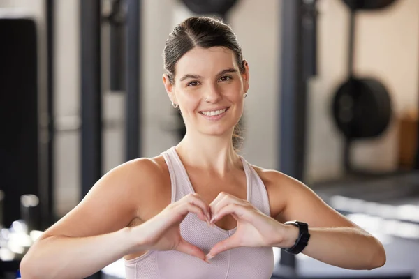 Portrait of smiling caucasian athlete showing heart shape sign and symbol during workout in gym. Strong, fit, active woman showing passion and love for exercise and training in health and sports club.