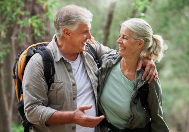 A senior caucasian couple smiling and looking happy in a forest during a hike in the outdoors. Man and wife showing affection and holding each other during a break in nature.