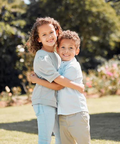 Portrait of a mixed race brother and sister smiling, standing and embracing each other in a garden outside. Hispanic Male and female siblings showing affection on a sunny day.