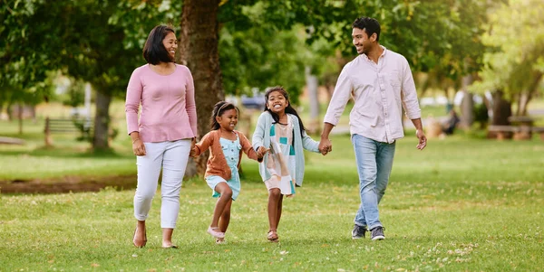 Young happy mixed race family holding hands and walking together in a park. Loving parents spending time with their little daughters in nature. Sisters bonding with their mom and dad outside.