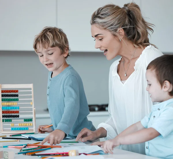 Caucasian mother helping son with homework. Proud mom looking at childs drawings learning about colours. Young mother at home with two sons. Kids using colouring pencils. Teacher tutor with little
