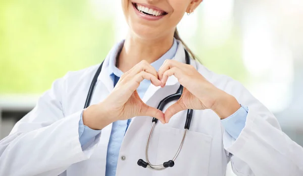 Unknown female mixed race doctor sitting in her office and showing a heart shape gesture with her hand in a hospital. Hispanic woman make a hand gesture at work.