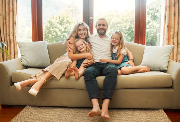 Young happy content caucasian family holding a cardboard as a roof covering them sitting on the floor at home. Cheerful little girls bonding with their mother and father. Loving parents spending time