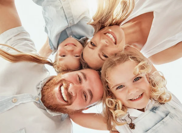 Bottom of happy family in a huddle. Faces of smiling mother and father with their cute daughters from below. Young woman and man having fun and playing with their little girls in a circle and hugging.