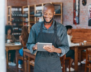 Young african american businessman wearing a apron working in a retail store using a digital tablet device. Portrait of a smiling small business owner, entrepreneur buying stock online using wireless
