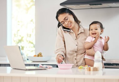 Dizüstü bilgisayarıyla çalışan ve bebeğini beslerken cep telefonuyla konuşan bir kadının fotoğrafı..