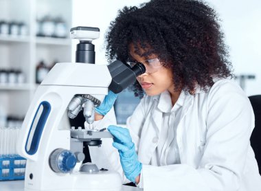 Labaratuarındaki mikroskopta tıbbi örneklere bakan gözlüklü Afro-Amerikalı genç bir kadın. Gözlük takan ve eldiven takan melez bir kadın bilim adamı araştırma yapıyor..