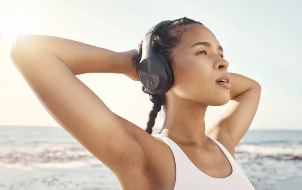 健康的年轻女运动员靠在一起 一边用耳机听音乐 一边休息 并将胳膊伸到脑后 — 图库照片