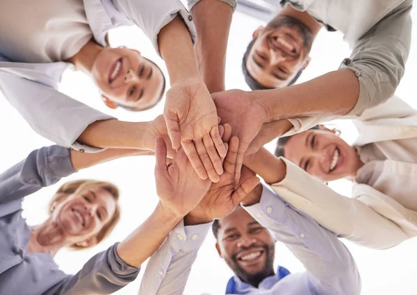 Low angle shot of a group of businesspeople joining their hands together in a huddle in an office.