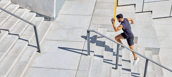 High angle shot of a sporty young man running up a staircase while exercising outdoors.