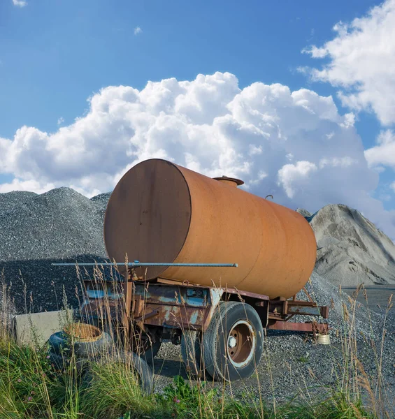 Old water tanker decaying at construction site. Rusted water container near a heap of concrete and cement. Abandoned old rusty water trailer tank near a pile of sand and gravel in building industry.