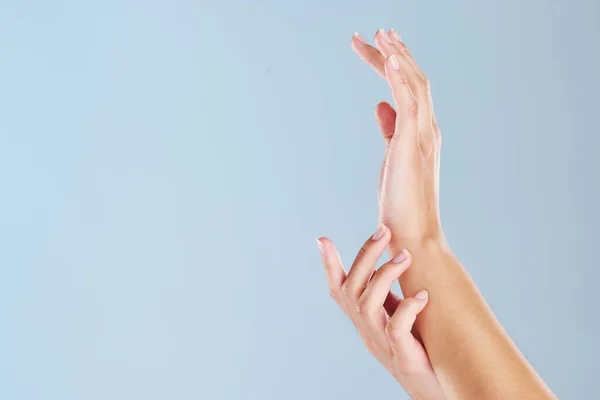 Closeup of a womans hands with a blue studio background and copyspace. Zoom in on manicured fingernails touching soft skin after using a beauty treatment or skin mask. Hand model with copy space.