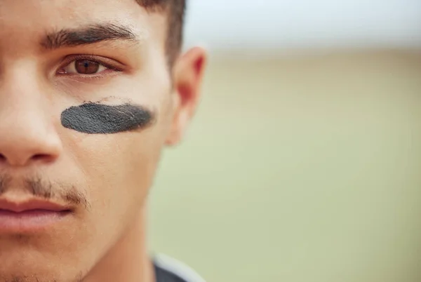 Portrait of a young male baseball player standing on a field with black paint markings on his face. Focused skilled sportsman, determined and motivated to have a competitive sporting game outside.