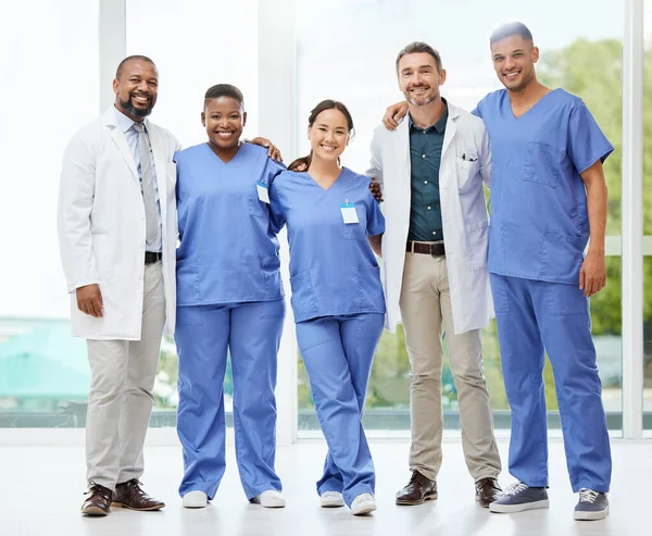 Shot of a cheerful group of doctors standing with their arms around each other inside of a hospital during the day.