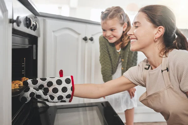 Shot of a mother and daughter putting a tray of cookies in the oven at home.
