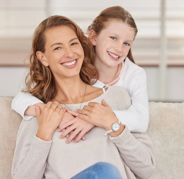 Portrait of a single mother and her daughter. Adorable girl bonding with her single parent and hugging in the living room at home. Smiling woman and her affectionate kid enjoying free weekend time.