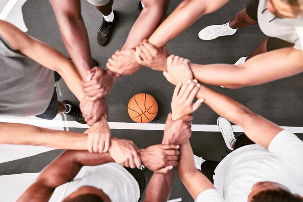 Athletes showing trust and standing united. Men expressing team spirit with their hands joined huddling at a basketball game. Sportsmen holding wrists in huddle for support and unity at sports match