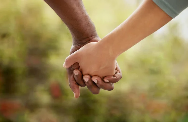 Closeup of biracial couple interlocking their fingers and holding hands while bonding in the garden at home. Mixed race woman united with African American man. Standing together in support and love.