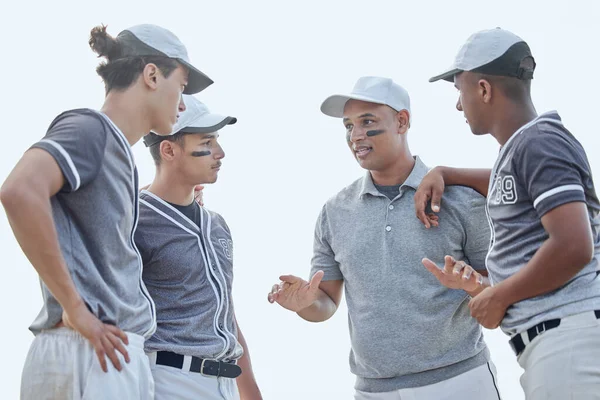 Baseball coach from below giving match pep talk and planning game strategy with group of players in huddle on sports pitch outside. Trainer encouraging and motivating team for tournament competition.