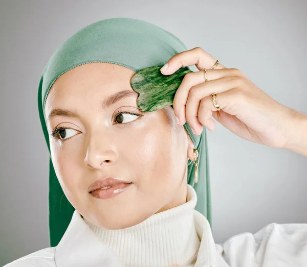 一个被用在年轻的穆斯林妇女脸上的瓜沙 在灰色的工作室背景下被隔离 头戴头巾或头巾的妇女 使用抗衰老工具减少皱纹 促进细胞更新 — 图库照片