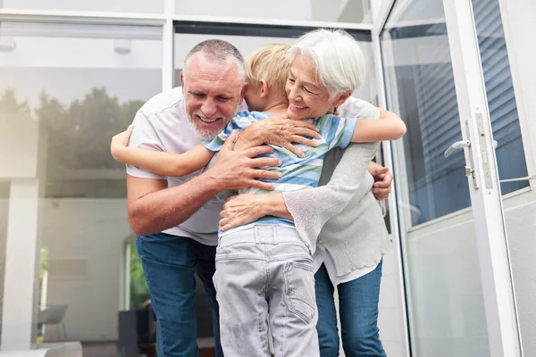 Senior grandparents hugging their small grandson at home. Little boy bonding and embracing smiling grandmother and grandfather. Adopted child feeling happy and grateful while hugging elderly couple.