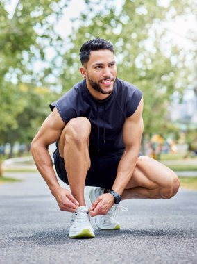 Shot of a sporty young man tying his laces while exercising outdoors.