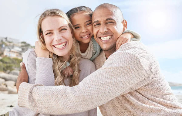 Smiling married couple bonding with daughter on the beach. Adopted little girl embracing her parents on a beachside vacation. Happy husband and wife enjoying free time with their child.