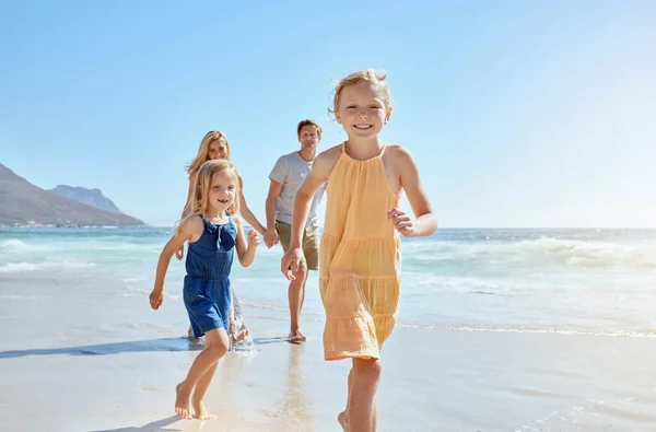 Joyful young family with two children running on the beach and enjoying a fun summer vacation. Two energetic little girls having a race while their mother and father follow in the background.