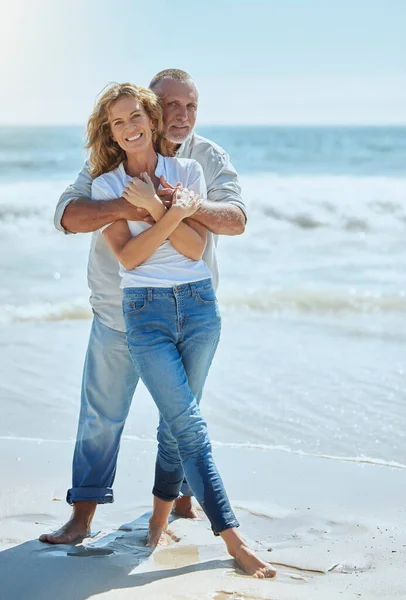 Portrait of a happy and loving mature couple enjoying a day at the beach in summer. Cheerful affectionate senior husband hugging his joyful wife while standing in the water on holiday.