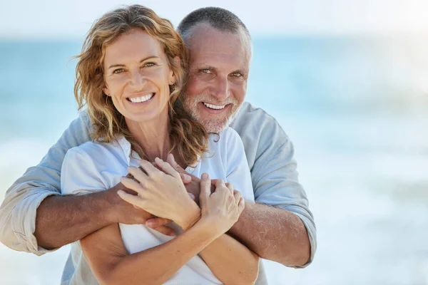 Portrait of happy and loving retired mature caucasian couple enjoying a romantic date at the beach on a sunny day. Cheerful affectionate husband hugging his wife while enjoying seaside vacation.