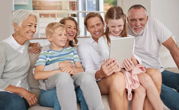 Happy family using a digital tablet in the living room at home. Cute little girl and boy bonding with parents and grandparents in the lounge. Watching a movie and using technology for a video call.