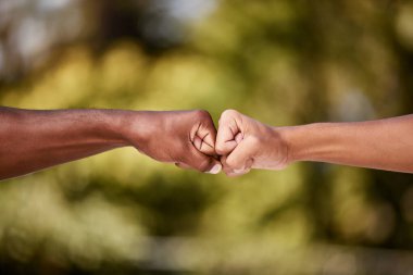 Fist bump of two interracial men outdoor against a blur background. Closeup of diverse athletes doing social gesture greeting in a park. Showing solidarity, friendship, brotherhood, teamwork or unity. clipart