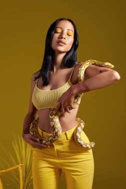 Sarı bir konsepti modellerken yılanı tutan şık bir kadının fotoğrafı..