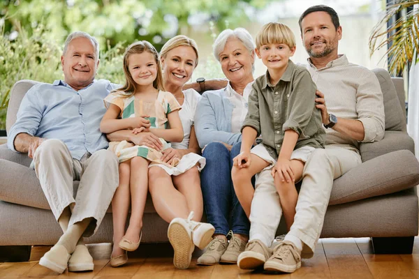 Portrait of a smiling multi generation caucasian family sitting close together on the sofa at home. Happy adorable children bonding with their mother, father, grandfather and grandmother on a weekend.