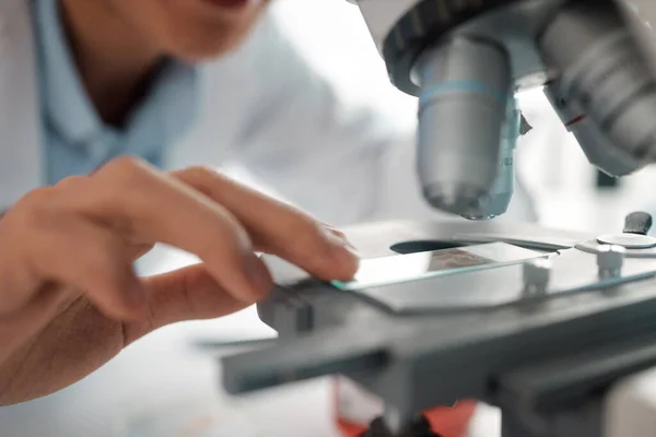 Shot of a male lab tech positioning a slide under a microscope.