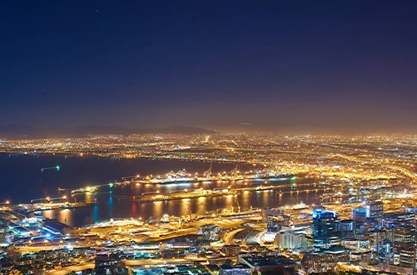 Copyspace with dark night sky over a cityscape and ocean view in Cape Town, South Africa. Scenic panoramic landscape of lights illuminating a metropolitan skyline in the city centre at night.