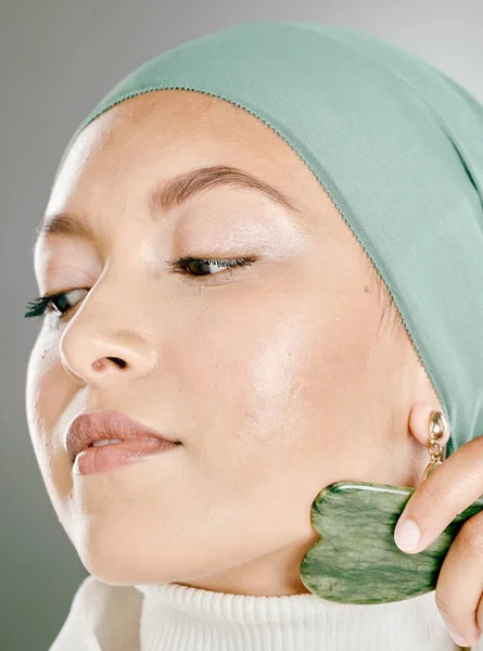 Woman using a facial stone on her face. Beauty model doing her morning skin care routine with a jade stone. Young female using a gua sha product for healthy skin