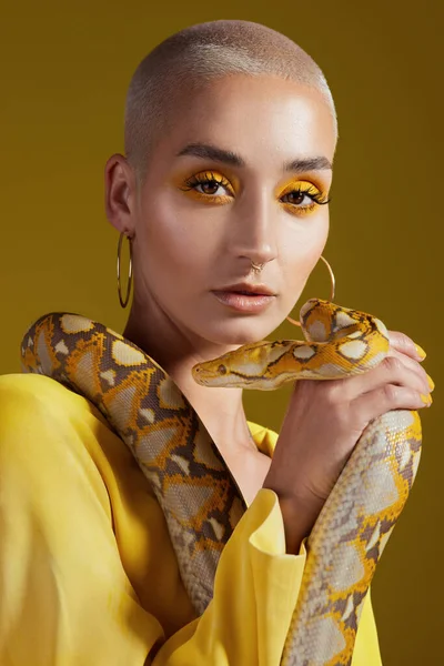 Shot of a fashionable woman holding a snake while modelling a yellow concept.