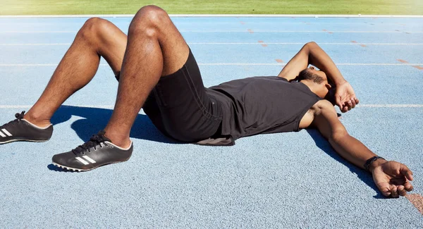 Closeup of a fit active young male athlete lying exhausted flat on the track after a race and feeling tired after a sprint on a running track. Male lacking energy after a hard workout practice run.